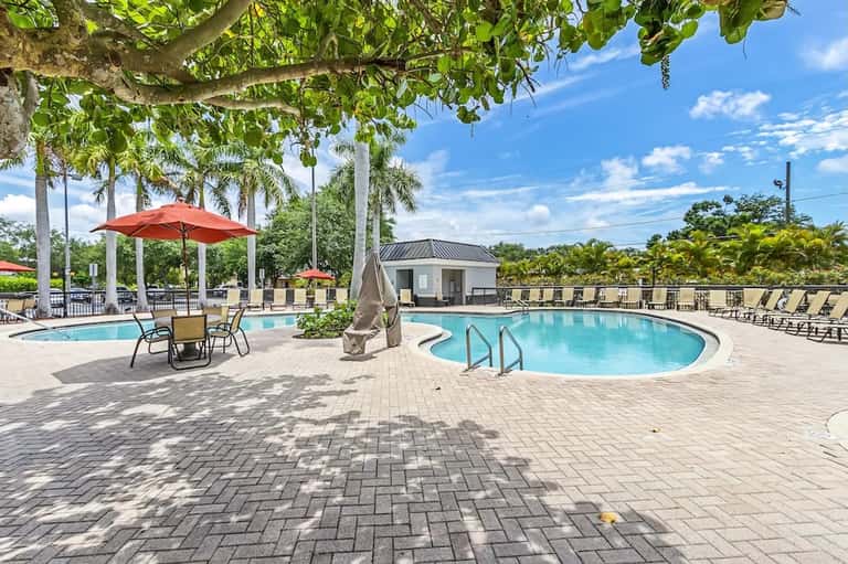 Resort courtyard with dual pools, red umbrellas, lounge seating, and mature palm trees
