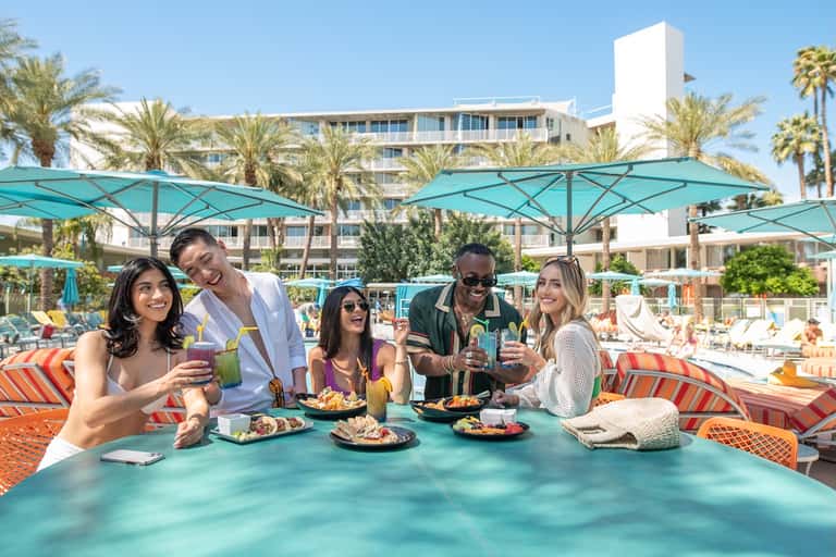 Beachfront resort guests enjoying cocktails under turquoise umbrellas with palm trees
