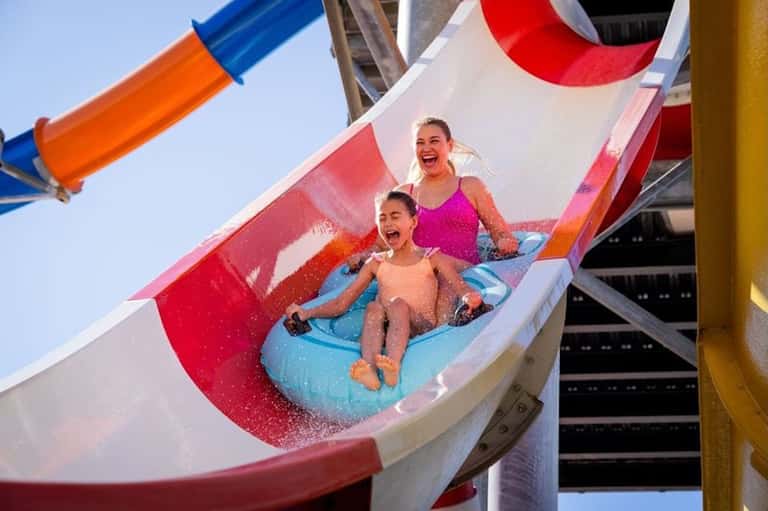 Children on colorful water slide at resort with red and white slide, clear blue sky