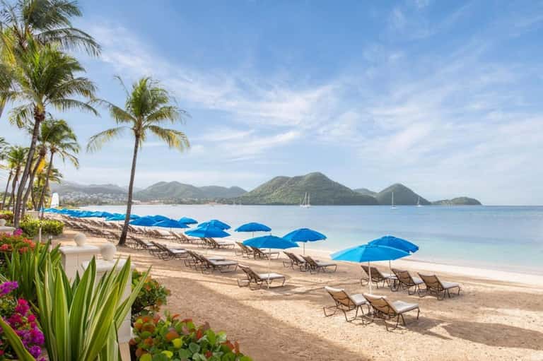 Tropical beach with blue umbrellas, lounge chairs, palm trees, and mountainous islands