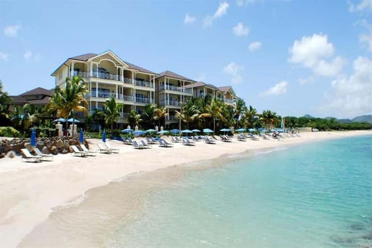 Beachfront resort with multi-story building, sandy beach, lounge chairs, palm trees, and turquoise Caribbean water