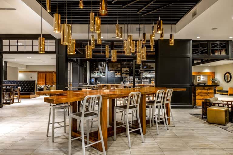 Modern hotel lobby bar with gold pendant lights, wooden counter, and contemporary seating