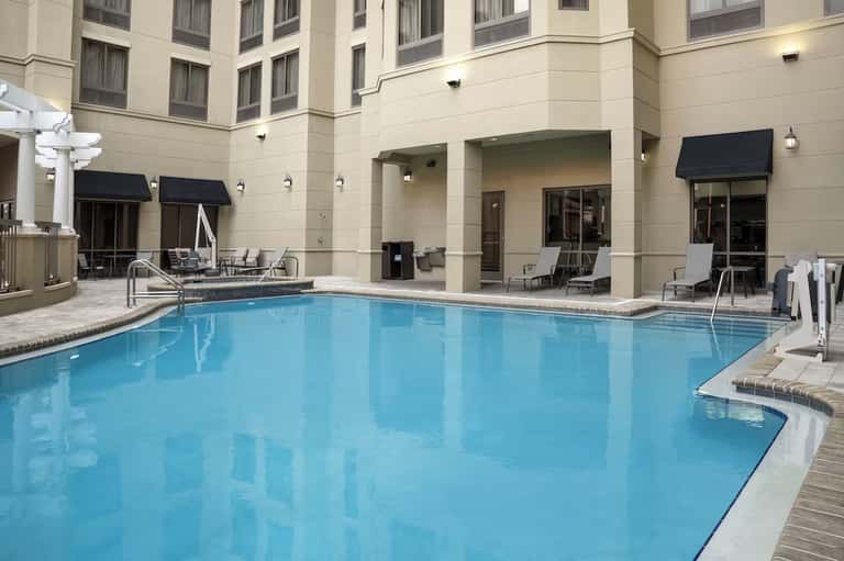 Indoor hotel pool with calm blue water, surrounding lounge chairs, hotel rooms, and covered patio area