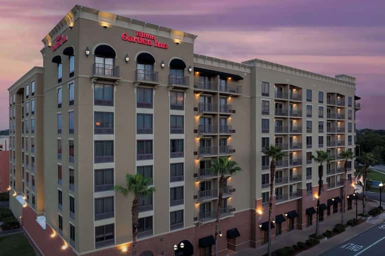 Hilton Garden Inn hotel exterior at dusk with illuminated facade and palm trees