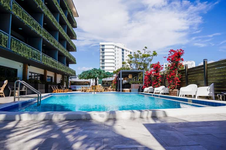 Outdoor swimming pool with white lounge chairs, flowering plants, and modern multi-story building