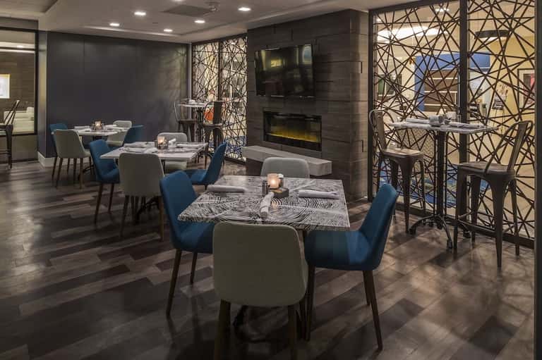 Contemporary dining room with blue chairs, patterned tables, fireplace, geometric window screens