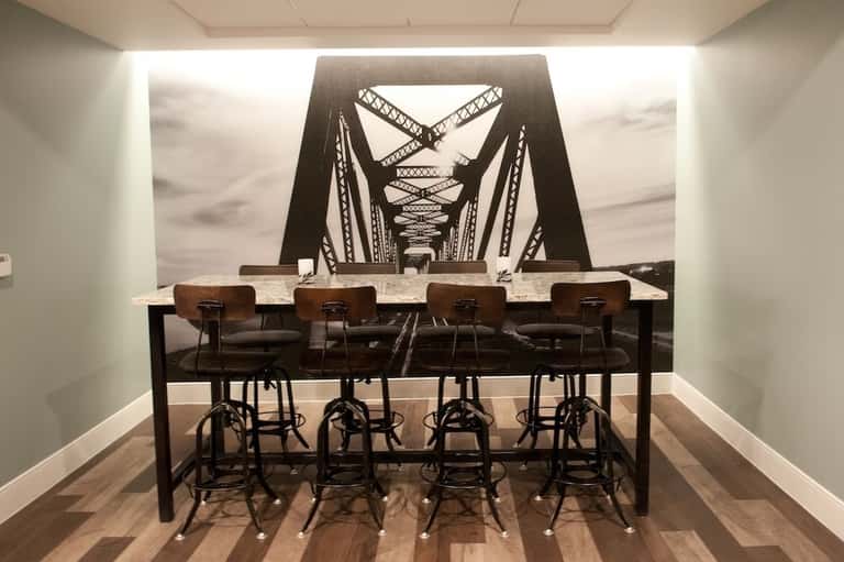 Conference room with high-top marble table, industrial-style chairs, and bridge mural