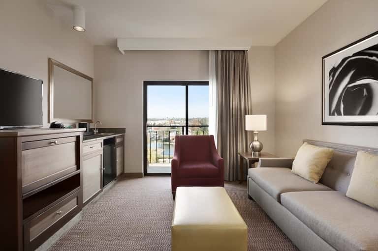 Hotel suite with sofa, kitchenette, TV, and balcony overlooking water