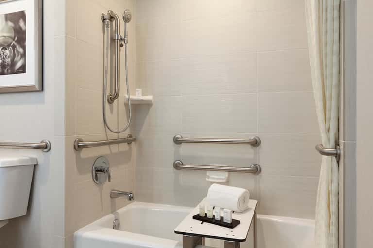 Accessible bathroom with grab bars, walk-in shower, and white tiled walls with safety features