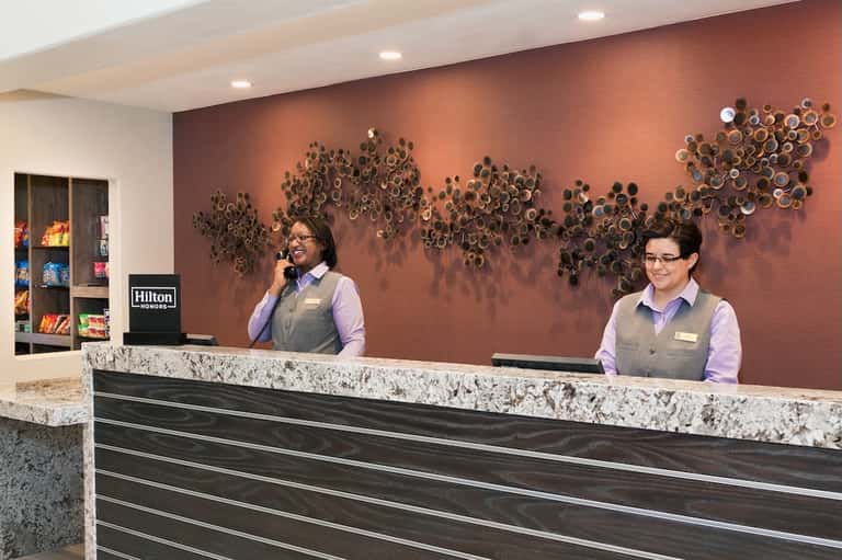 Hotel front desk with two staff members in uniforms, marble counter, and decorative wall art