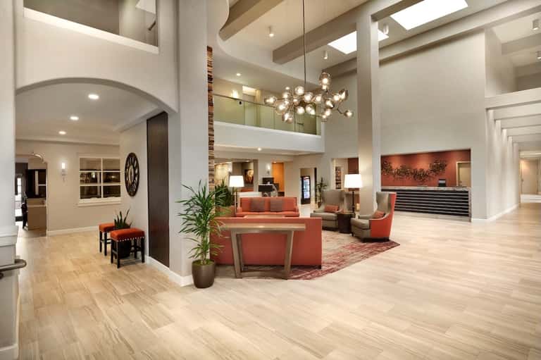 Spacious hotel lobby with high ceilings, modern chandelier, coral accent furniture, and open floor plan