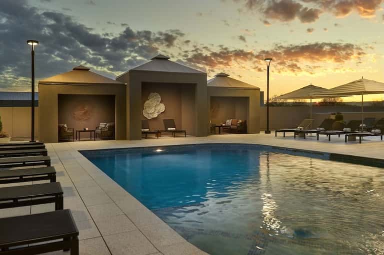 Modern resort pool with architectural pavilions, lounge chairs, and sunset lighting