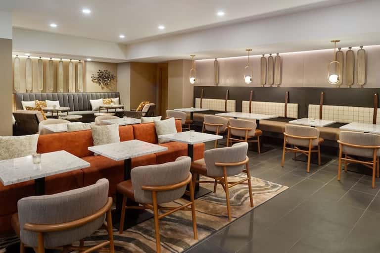 Contemporary hotel lounge with orange and gray seating, pendant lighting, and modern design elements