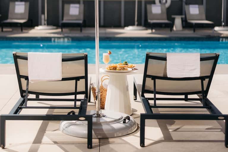 Two lounge chairs by resort pool with umbrella, food, and beverage service setup