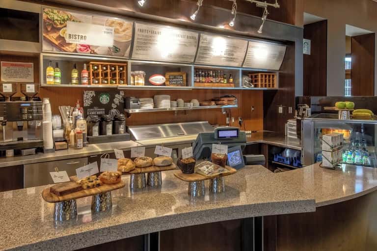 Starbucks cafe counter with menu boards, pastries, beverages, and espresso machine in bright setting