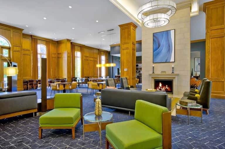 Elegant lobby with fireplace, golden wood columns, lime-green accent chairs, and modern chandelier lighting
