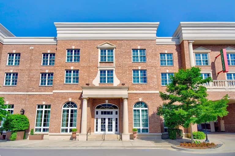 Historic red brick building facade with classical columns, blue windows, and manicured landscaping