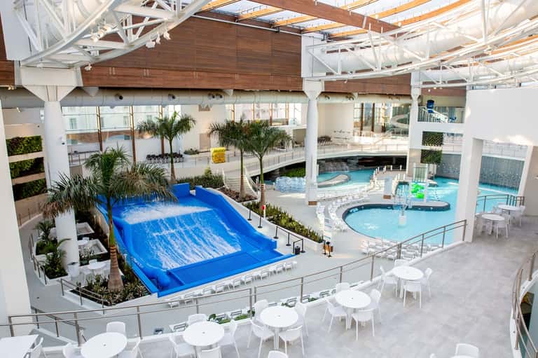 Indoor water park with blue wave slide and multiple pools under white ceiling