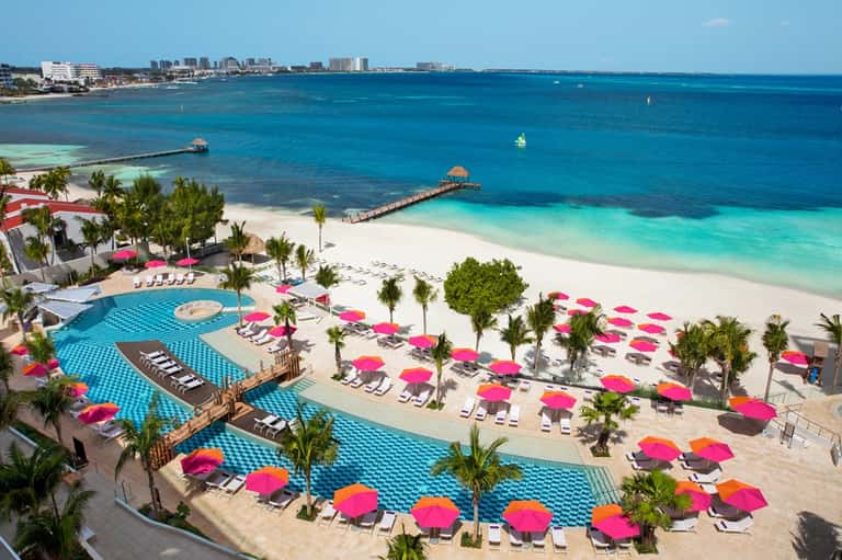 Aerial view of beachfront resort with turquoise pools, pink umbrellas, and ocean