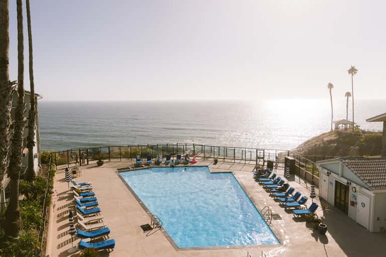 Resort pool deck with blue loungers, palm trees, and sparkling ocean horizon at sunset