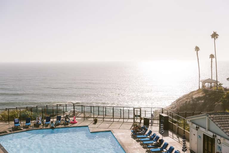 Coastal resort pool overlooking the Pacific Ocean with palm trees and cliffside gazebo