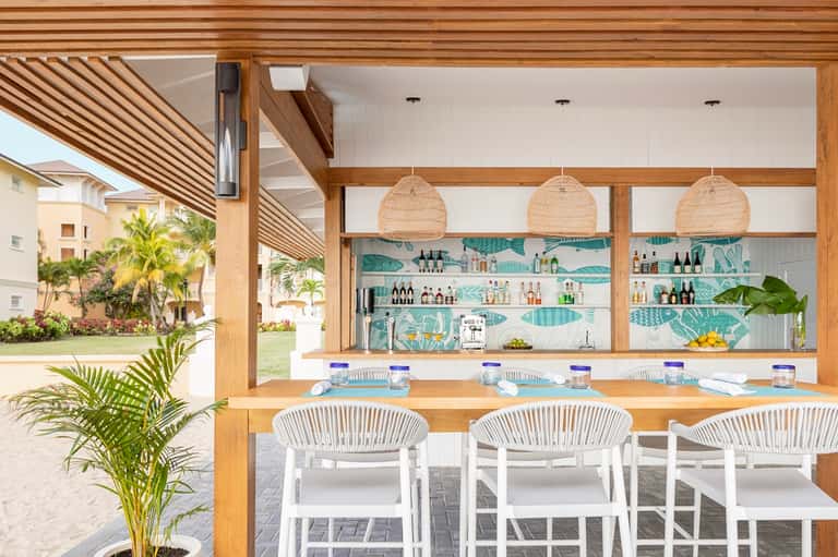 Outdoor bar and lounge with wooden beams, woven pendant lights, and beach access