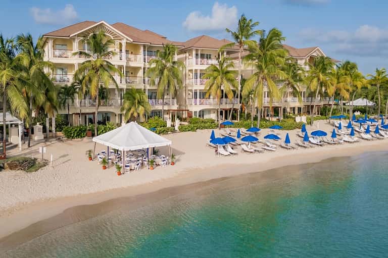 Beachfront resort building with palm trees, blue umbrellas, and sandy beach access