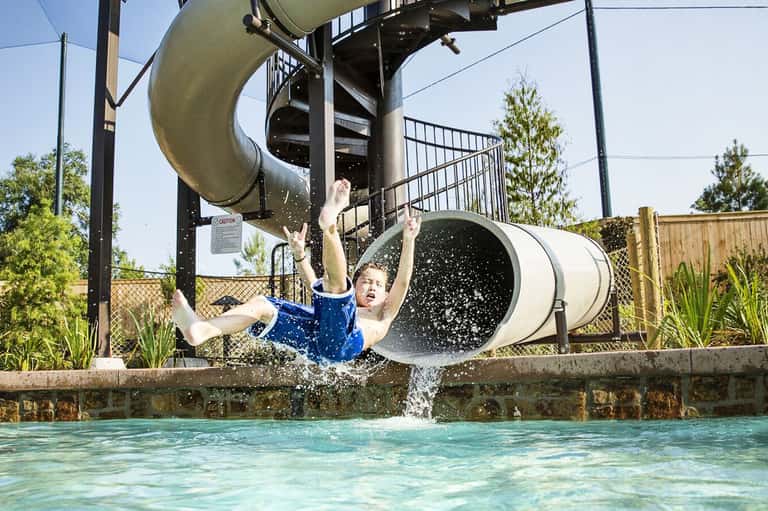 Child splashing down water slide into pool at recreational water park facility