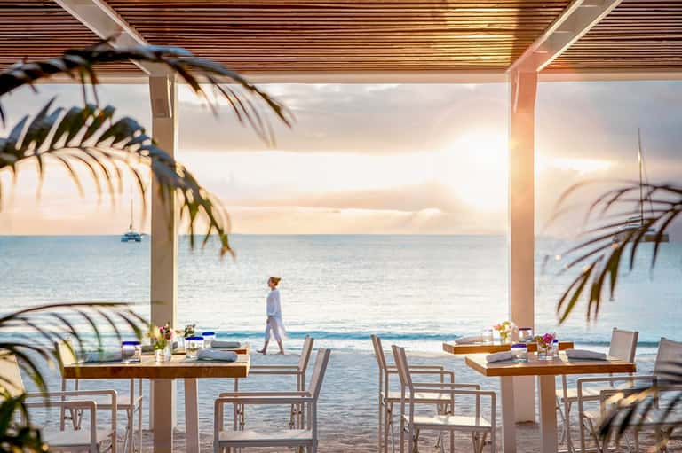 Oceanfront beachside dining pavilion at sunset with wooden tables and palm fronds