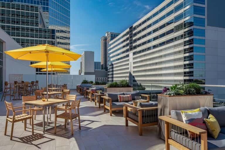 Rooftop lounge with yellow umbrellas, modern seating, city skyline views, and daybed pods