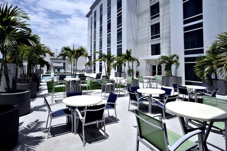 Modern courtyard with lounge seating, palm trees, white building facade, and sunny patio area