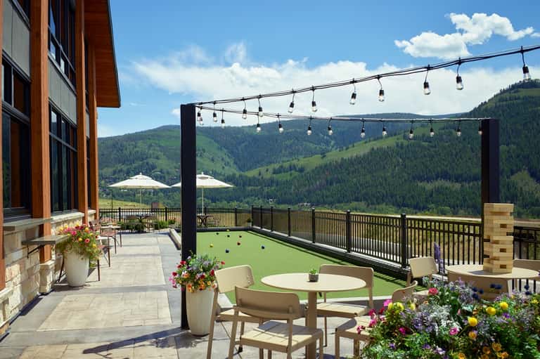 Mountain resort terrace with dining area, hanging lights, scenic valley views, and flowers
