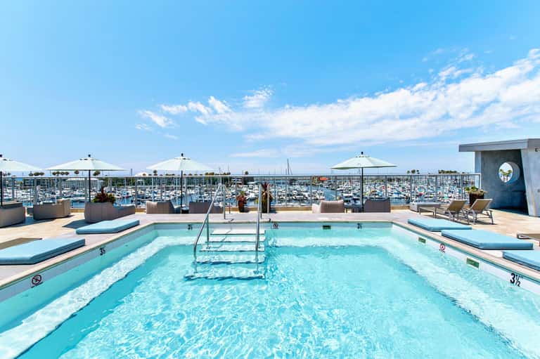 Rooftop swimming pool with marina views and white umbrellas on sunny day