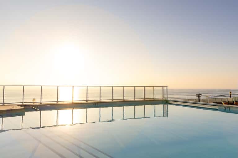 Oceanfront infinity pool reflecting sunset sky with metal railing and sea view