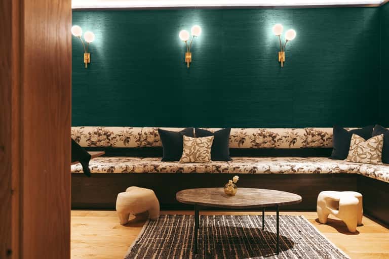 Contemporary lounge with deep teal accent wall, floral patterned bench seating, wooden table, brass wall sconces