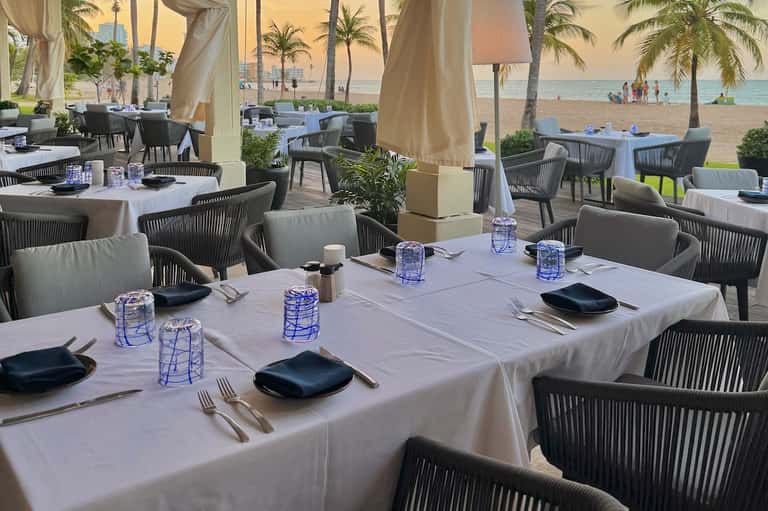 Elegant beachfront dining area with white tablecloths, dark chairs, and ocean view