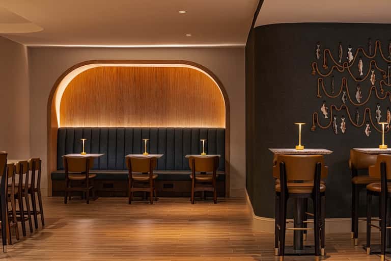 Upscale lounge bar with curved banquette seating, wood and black accents, and elegant pendant lighting