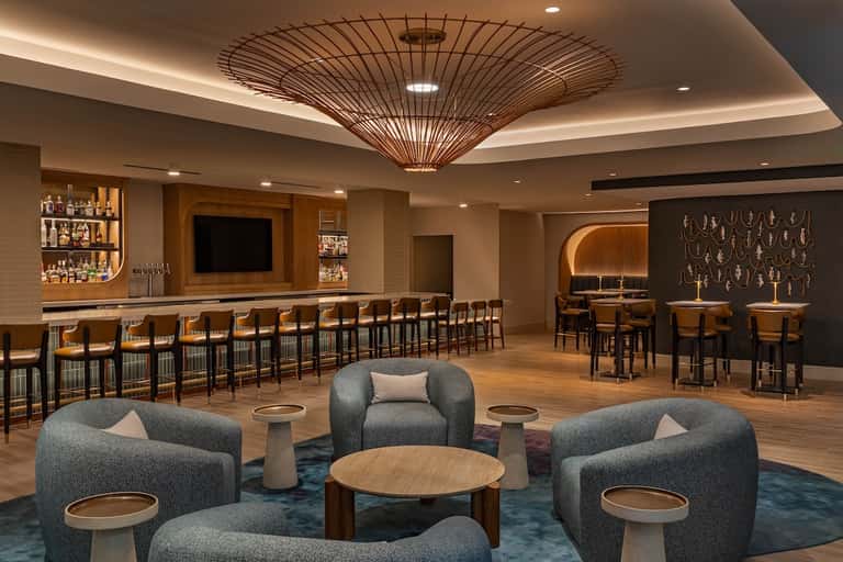 Upscale hotel lounge with bar seating, modern furniture, and decorative ceiling fixture
