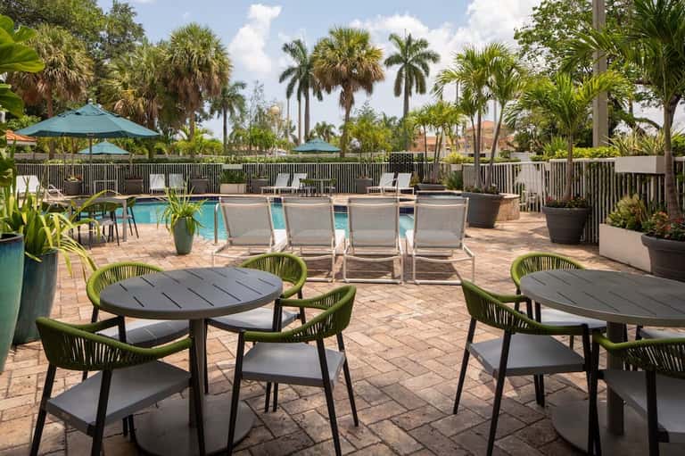 Tropical resort pool deck with lounge chairs, dining tables, umbrellas, and palm trees