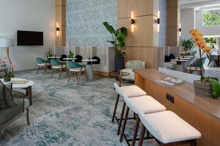Contemporary hotel lobby lounge with wooden accents, teal seating, plants, and modern lighting