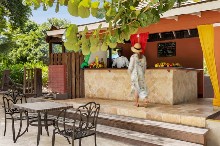 Outdoor tiki bar with orange awning, palm trees, and colorful arrangements on serving counter