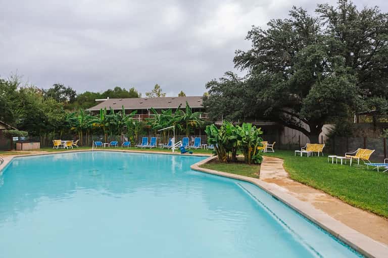 Resort pool surrounded by lush green lawns, banana plants, lounge chairs, and main building
