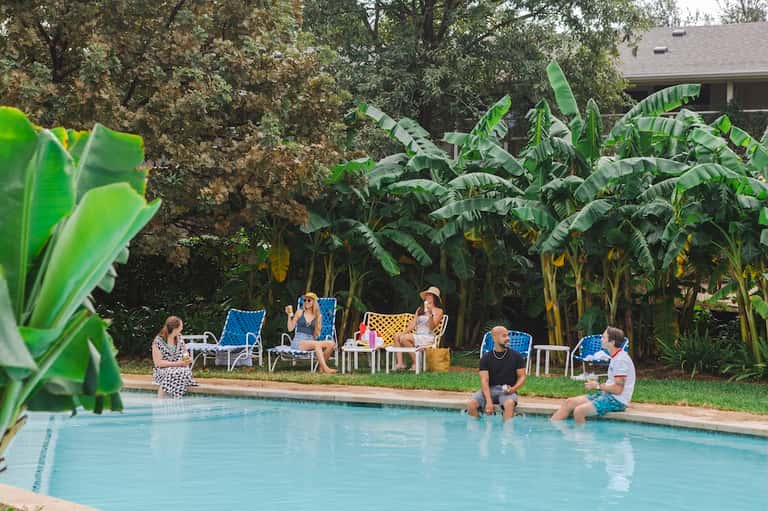 Resort pool with tropical landscaping, banana plants, and guests enjoying poolside lounge chairs