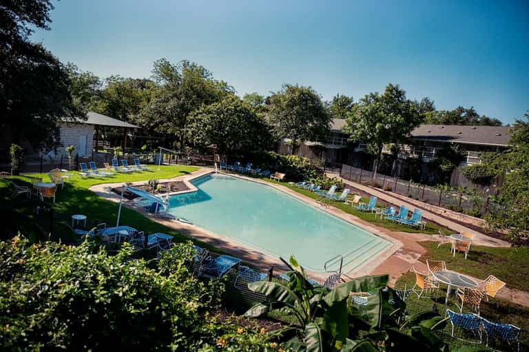 Rectangular resort pool with lounge chairs surrounded by mature trees and landscaping