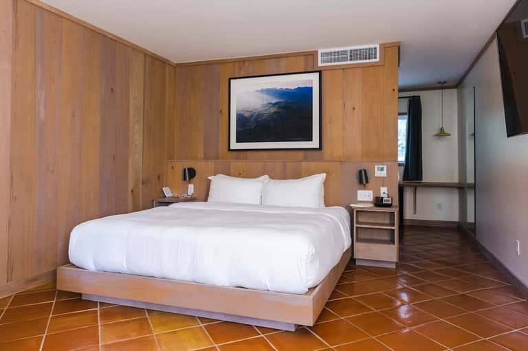Minimalist bedroom with wooden walls, white bedding, and mountain landscape artwork