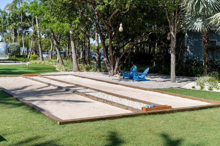 Cornhole game on resort grounds under palm trees near waterfront seating area