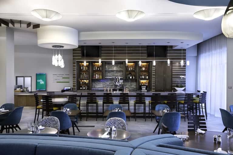 Modern hotel bar and lounge with black seating, pendant lights, and backlit liquor shelves