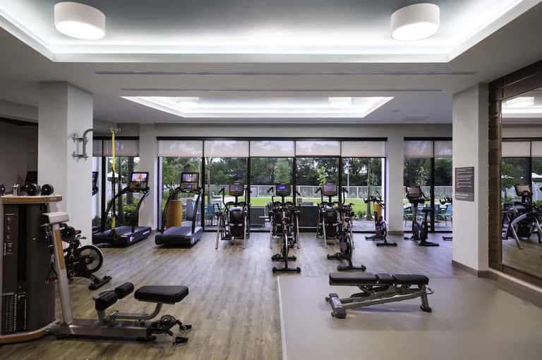 Modern fitness center with cardio equipment, stationary bikes, treadmills, and large windows overlooking grounds