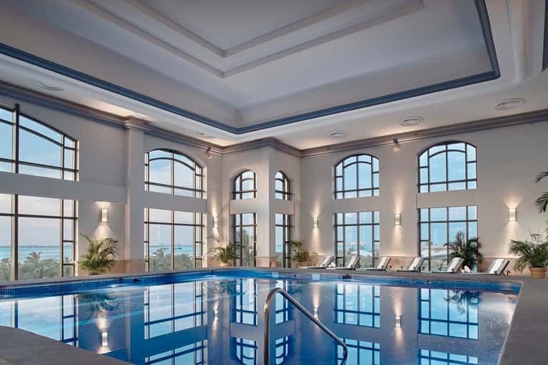 Elegant indoor pool with arched windows, white coffered ceiling, and ocean waterfront views