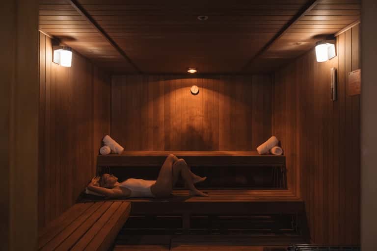 Wooden sauna interior with two-tier benches, ambient lighting, and rolled towels